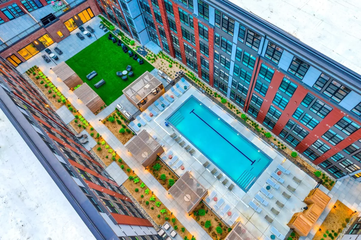 Aerial view of courtyard with pool, green lawn, and wood cabanas.