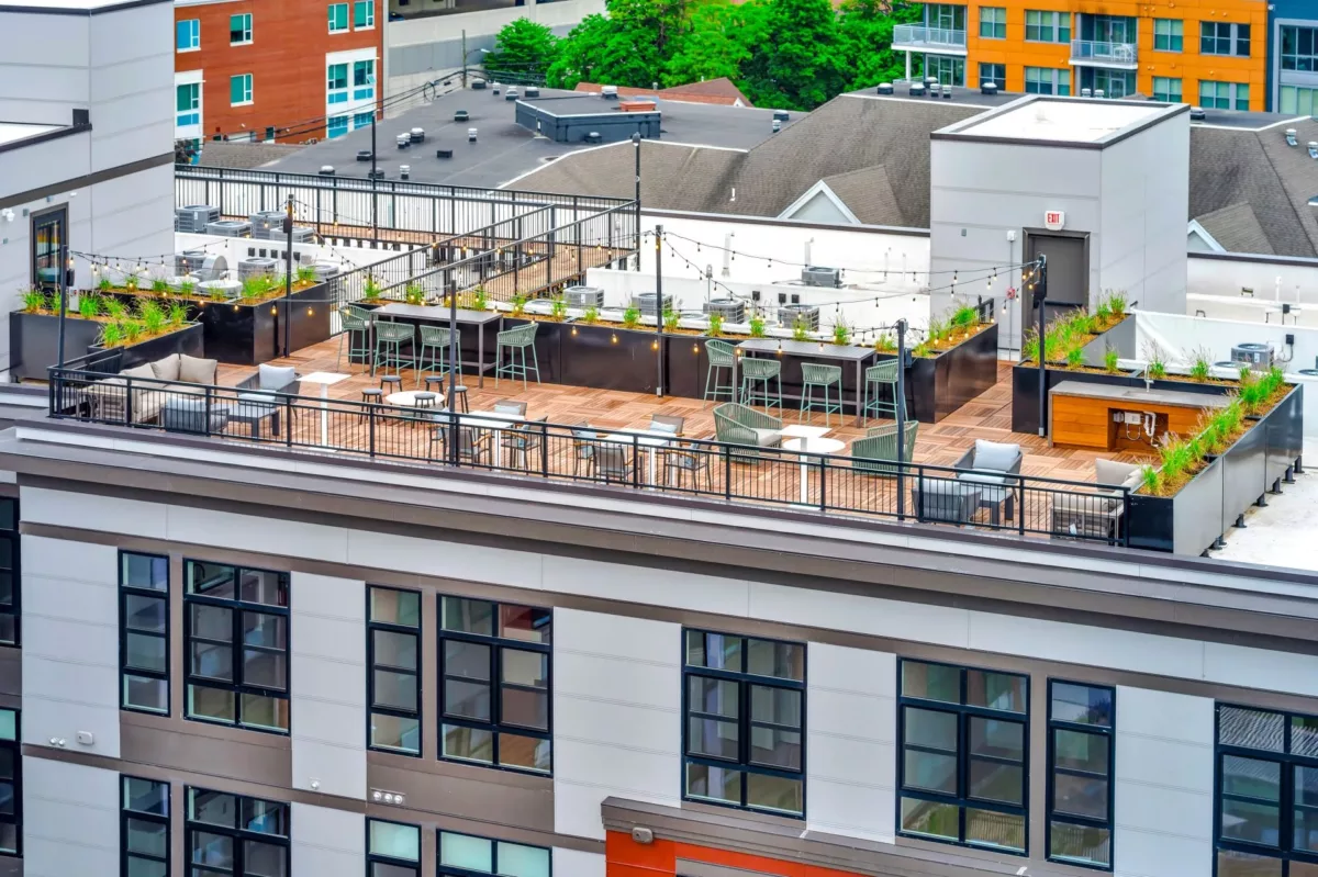 Rooftop lounge with tables, bar seating, and surrounding planters.