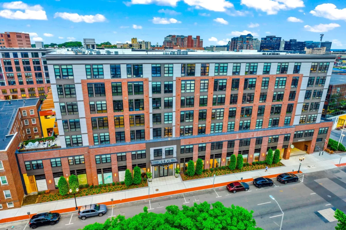 Exterior view of an apartment community with brick façade and trees and a sign over the entrance that says "Julius".