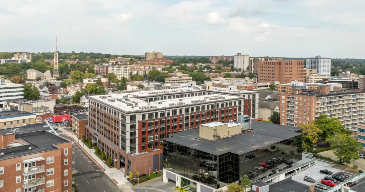 A drone shot with a red brick apartment building in the foreground and a city in the background.